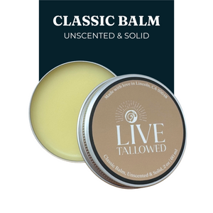 Live Tallowed Classic Balm, Unscented & Solid, in a 2 oz metal tin with the lid slightly open, revealing the smooth, golden balm inside. Label includes 'Made with love in Lincoln, CA.' Displayed on a clean background with bold text highlighting product details